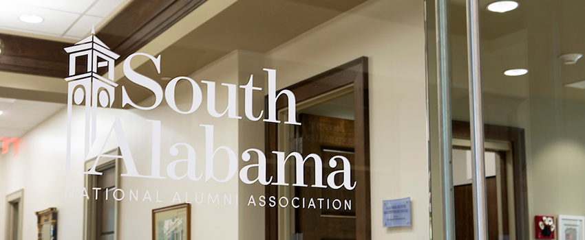Glass door of Alumni offices with South Alabama National Alumni Association logo on window.